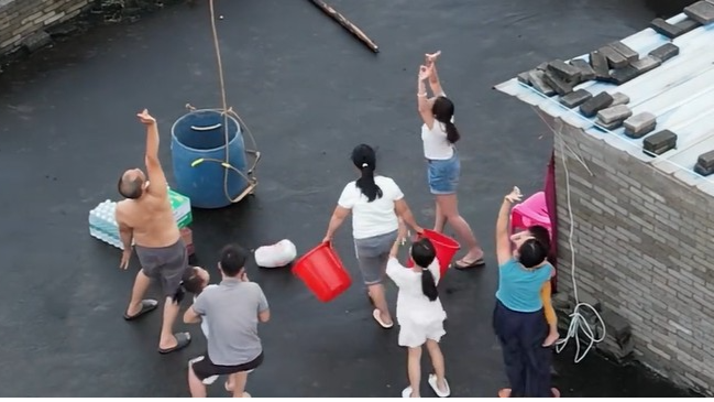 村民被洪水围困在房顶，救援人员用吊运机投放物资，村民抱拳致谢